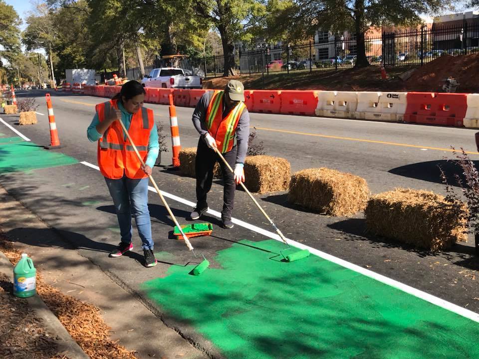 Two people in vests painting a sidewalk